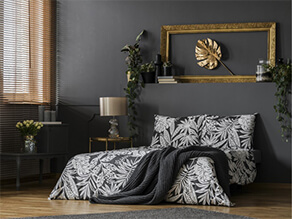 Dark grey feature wall bedroom with wooden floor and gold artwork plants and white bedding pillows
